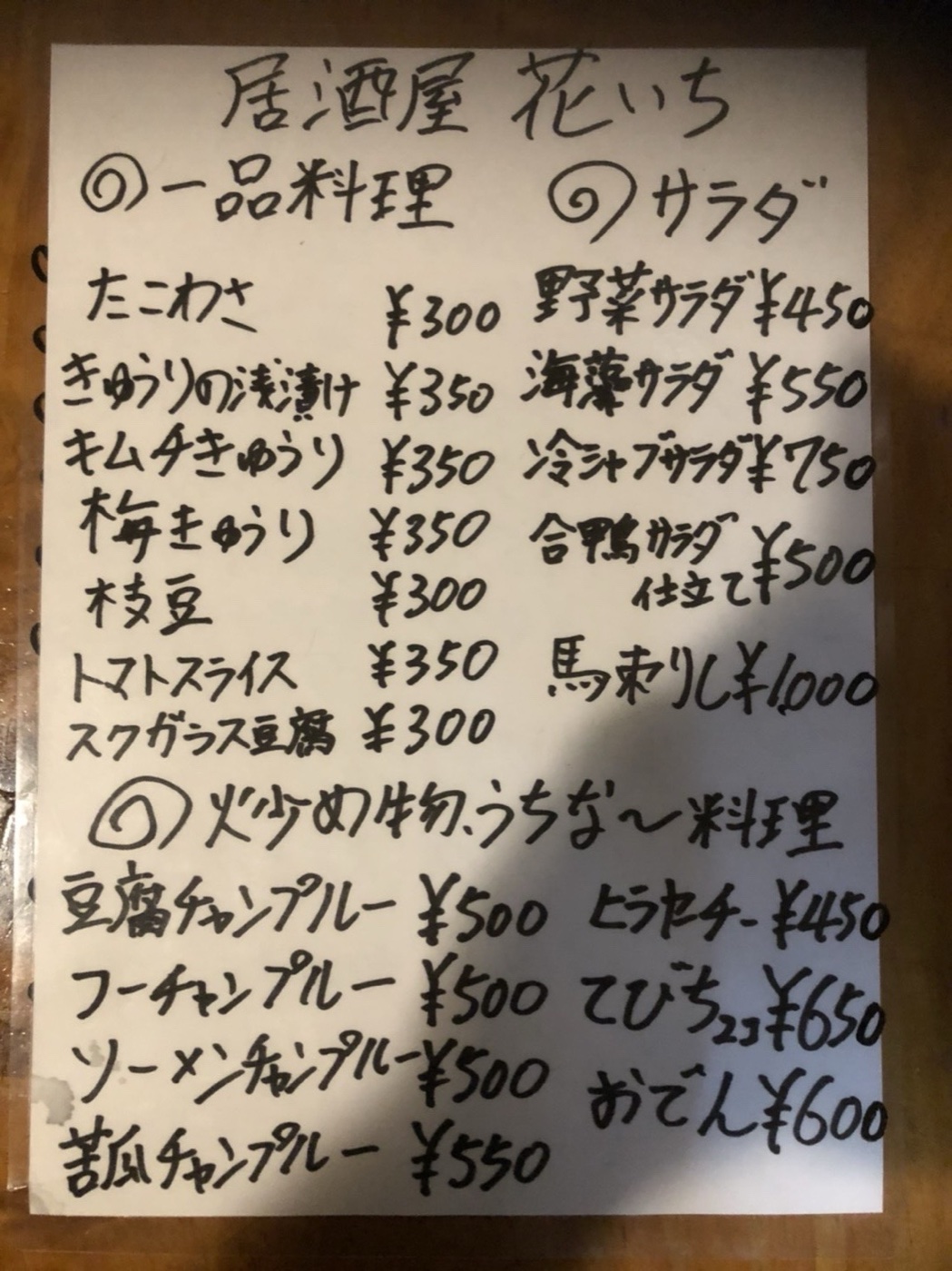 店内に貼られた手書きのお品書き。一品料理・サラダ・炒め物とうちなー料理の品名と価格が書かれている