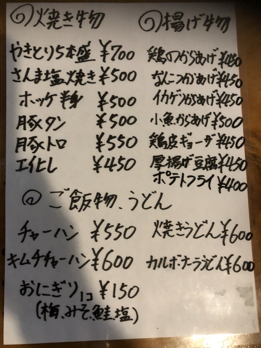 店内に貼られた手書きのお品書き。焼き物・揚げ物・ご飯物うどんの品名と価格が書かれている